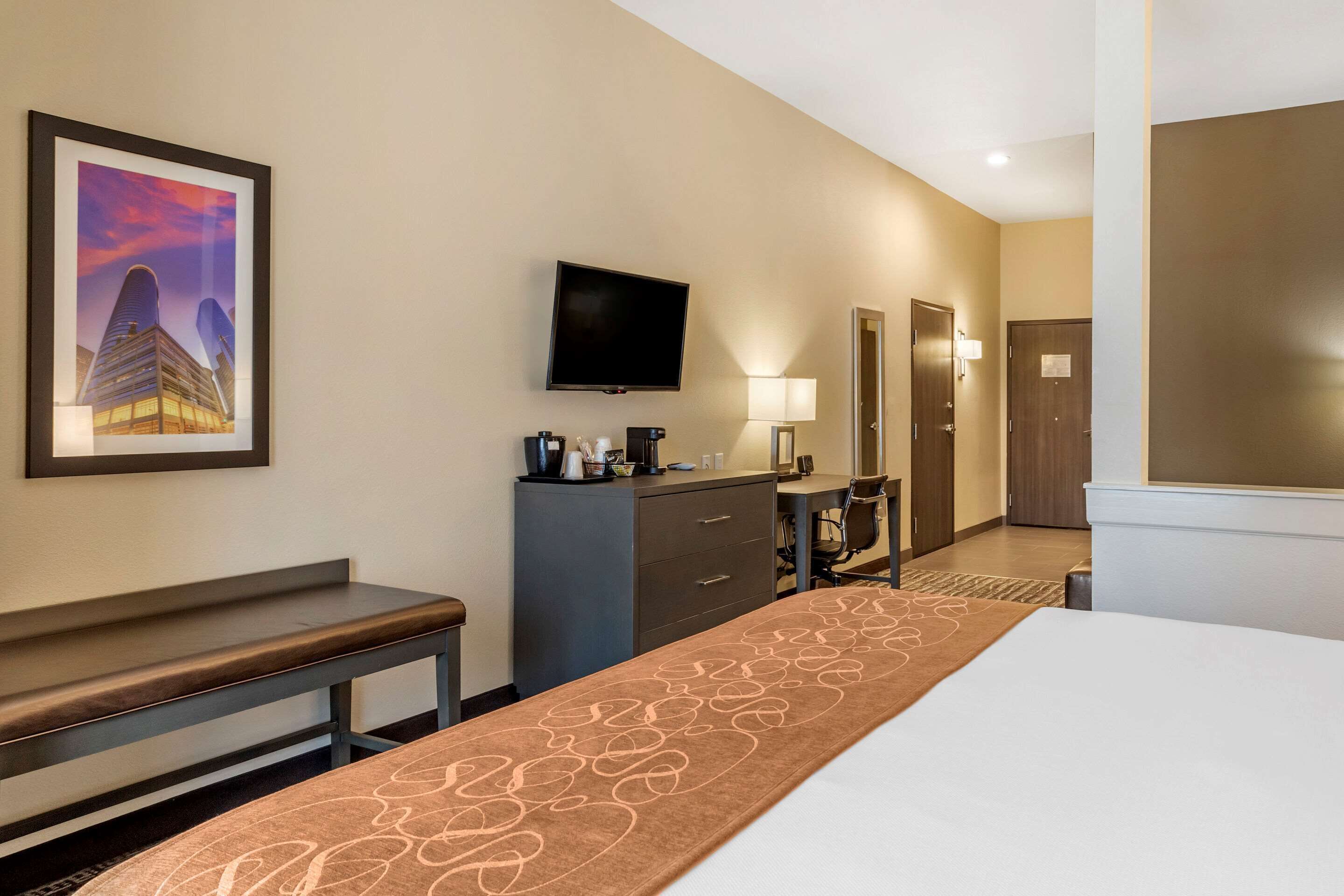 A hotel room with a bed, a desk, a chair, a television, a coffee maker, and a framed picture on the wall.