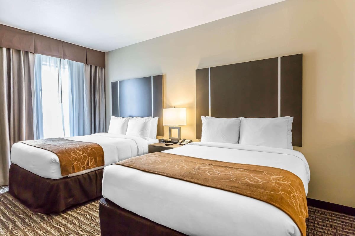 Une chambre d’hôtel avec deux lits, une table de chevet, une lampe et une fenêtre avec des rideaux.