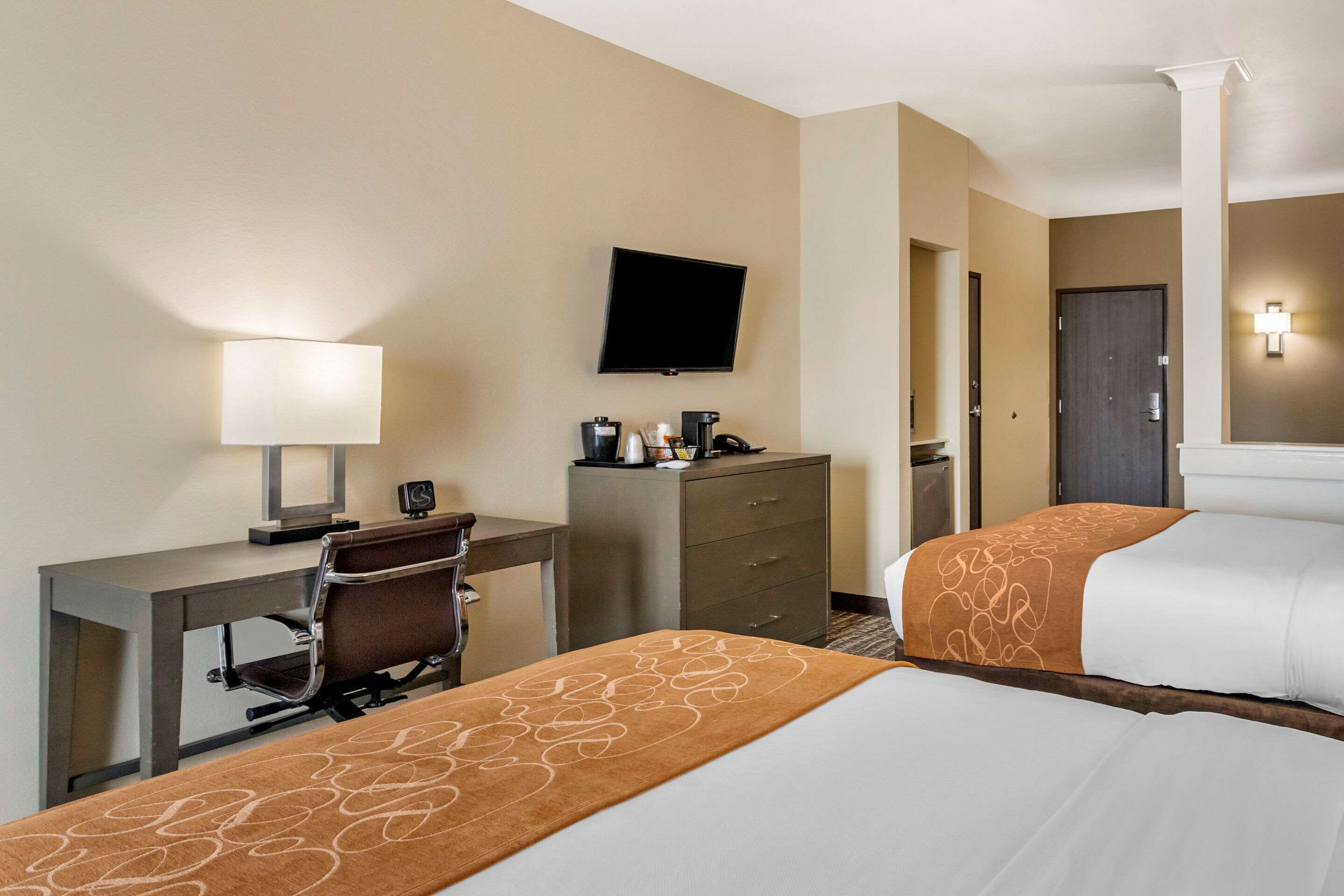 A hotel room with two beds, a desk with a chair, a television, a coffee maker, and a nightstand.