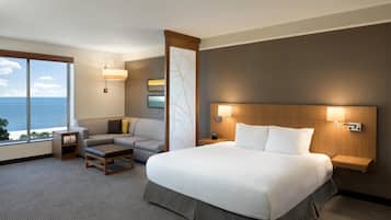 A hotel room with a large bed, a sofa, a small table, and a view of the ocean.