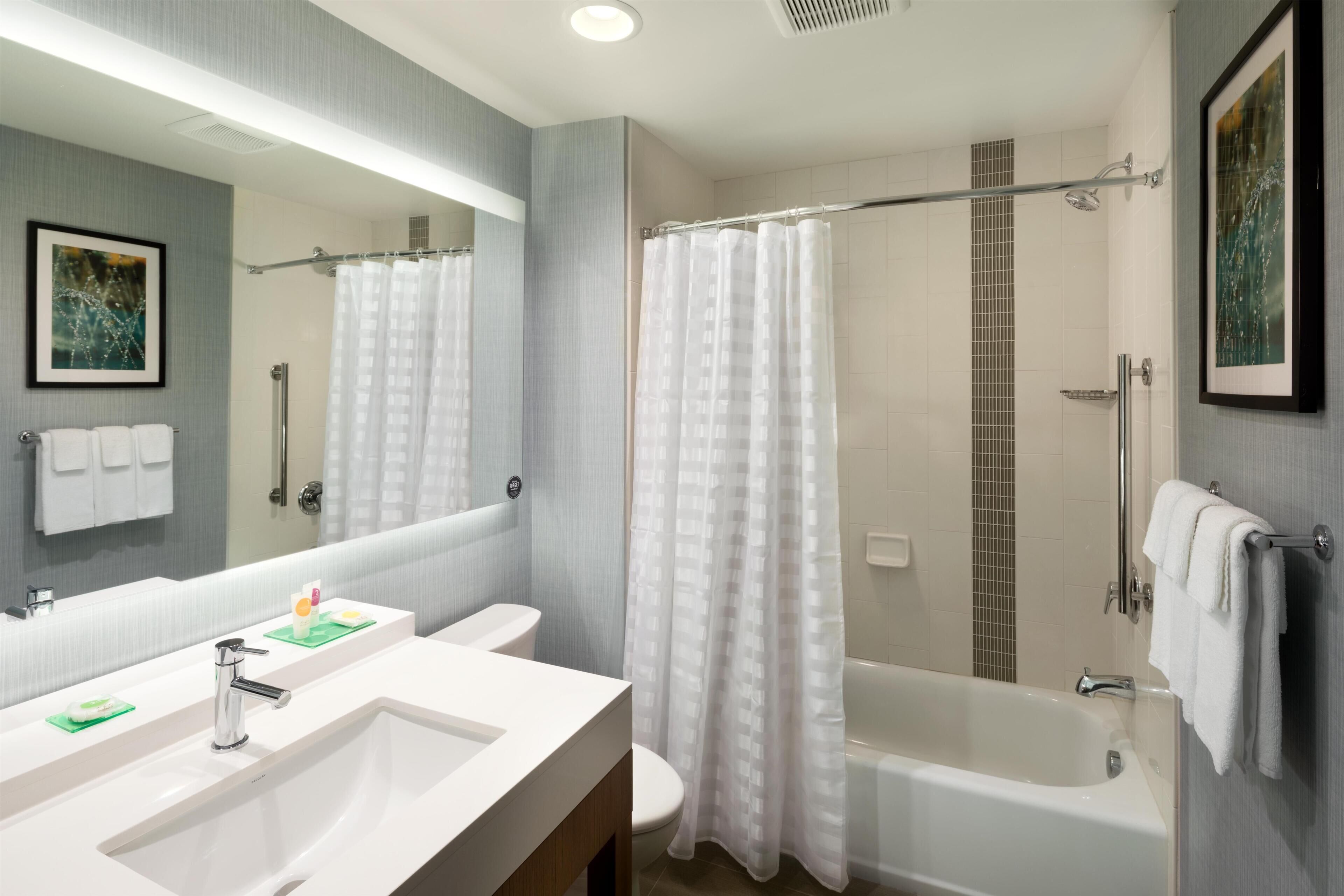A bathroom with a large mirror, two sinks, a toilet, a bathtub, and a shower curtain.