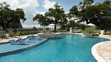 Relax by the serene pool surrounded by lounge chairs and a hot tub, set amidst mature trees for a peaceful ambiance.
