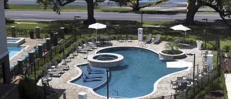 A pool area with lounge chairs, a hot tub, and a fire pit.