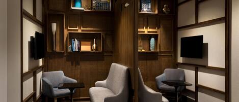 A room with two armchairs, a small table, a flat-screen TV, and shelves with decorative items.