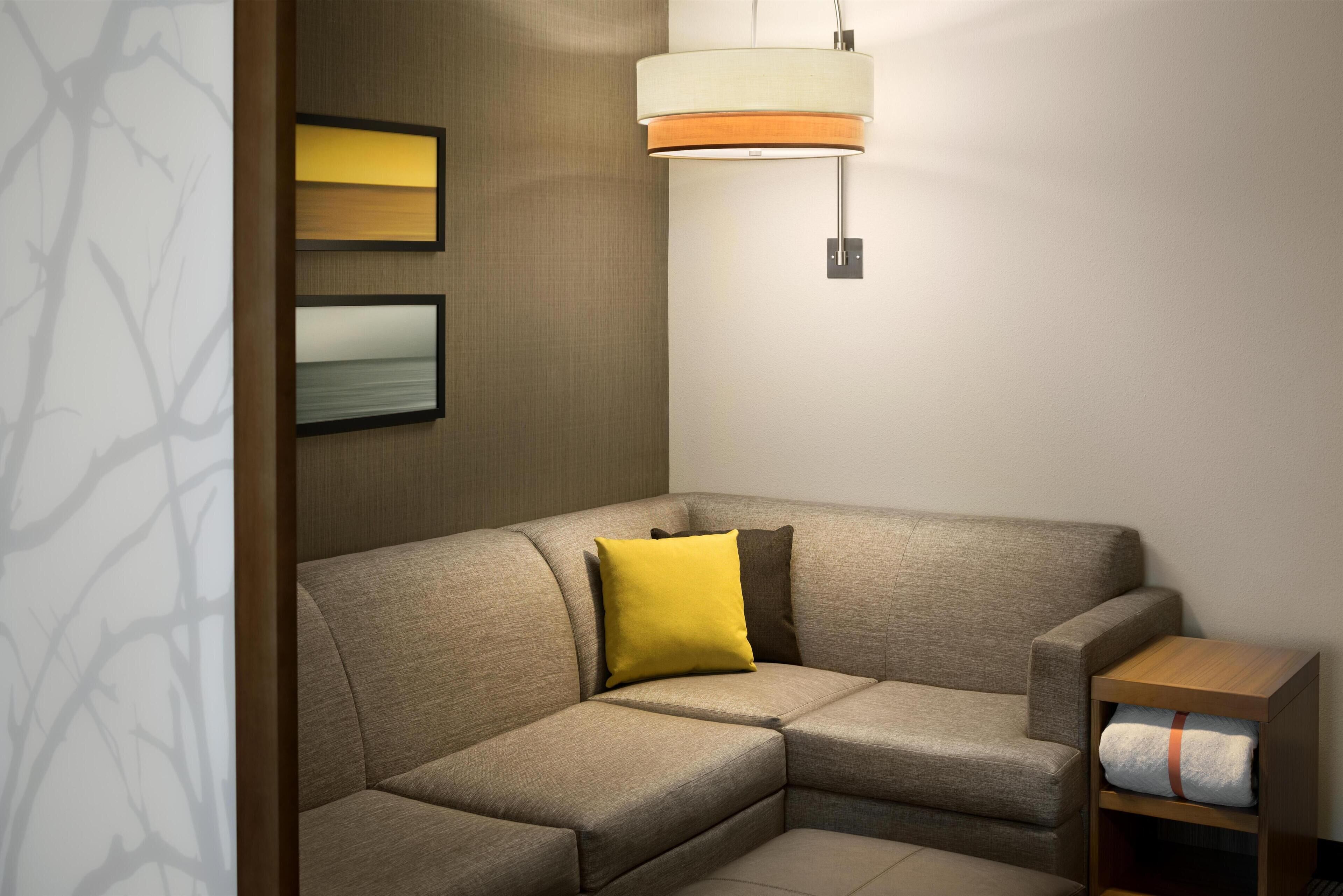 Ein Ecksofa mit Kissen, eine Wandleuchte und ein kleiner Holztisch mit einem Handtuch.