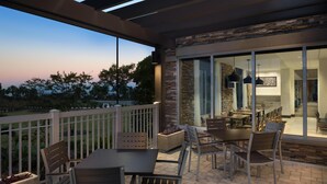 Un patio al aire libre con una mesa y sillas, un muro de piedra y vista al área de comedor interior.