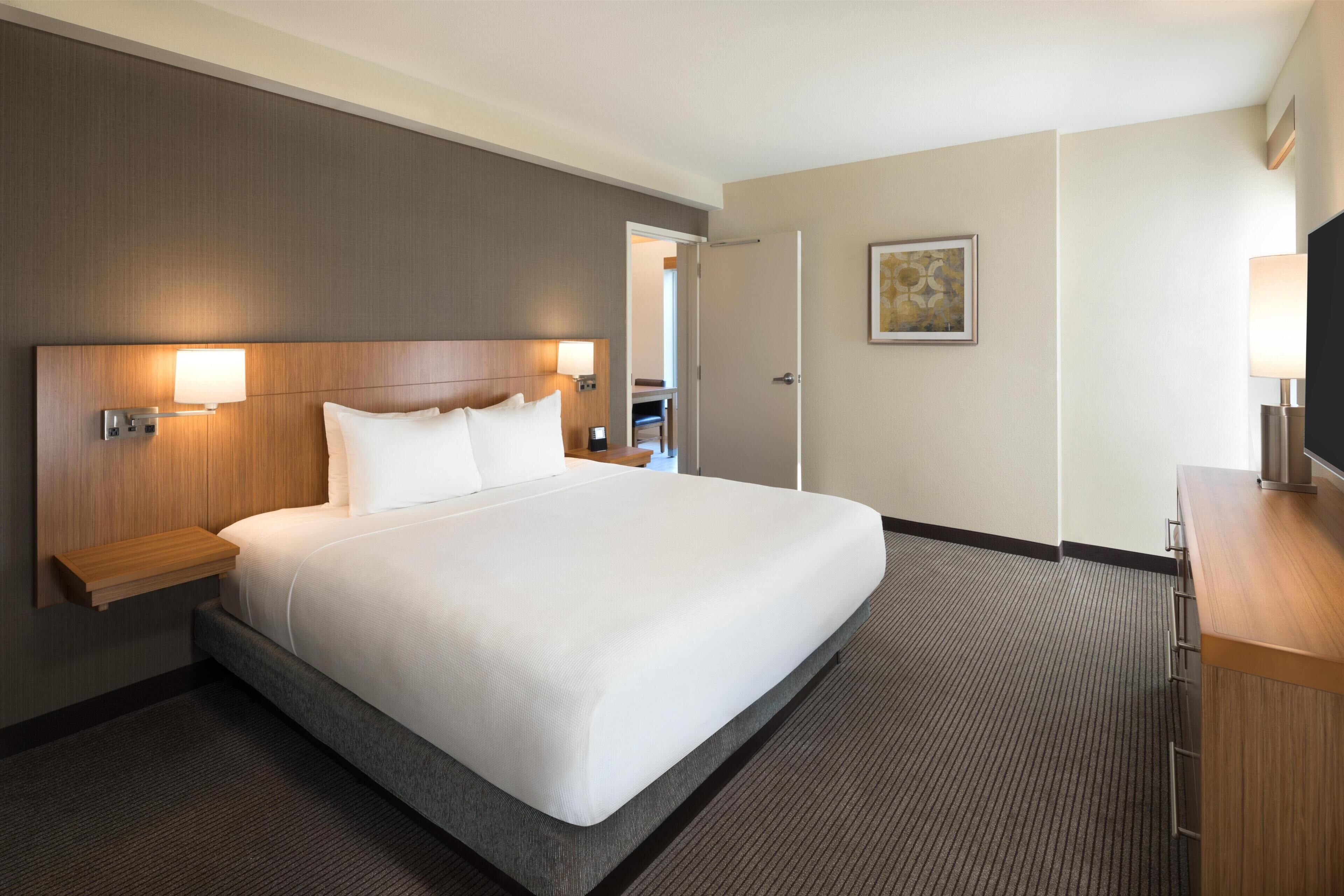 A hotel room with a large bed, bedside tables, a desk, and a television.