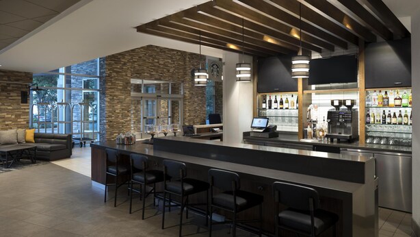 Un área de bar moderna con pared de piedra, taburetes, una máquina de café y un televisor.