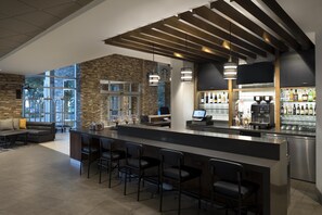 A modern bar area with a stone wall, bar stools, a coffee machine, and a television. - Hyatt Place Biloxi (Biloxi)