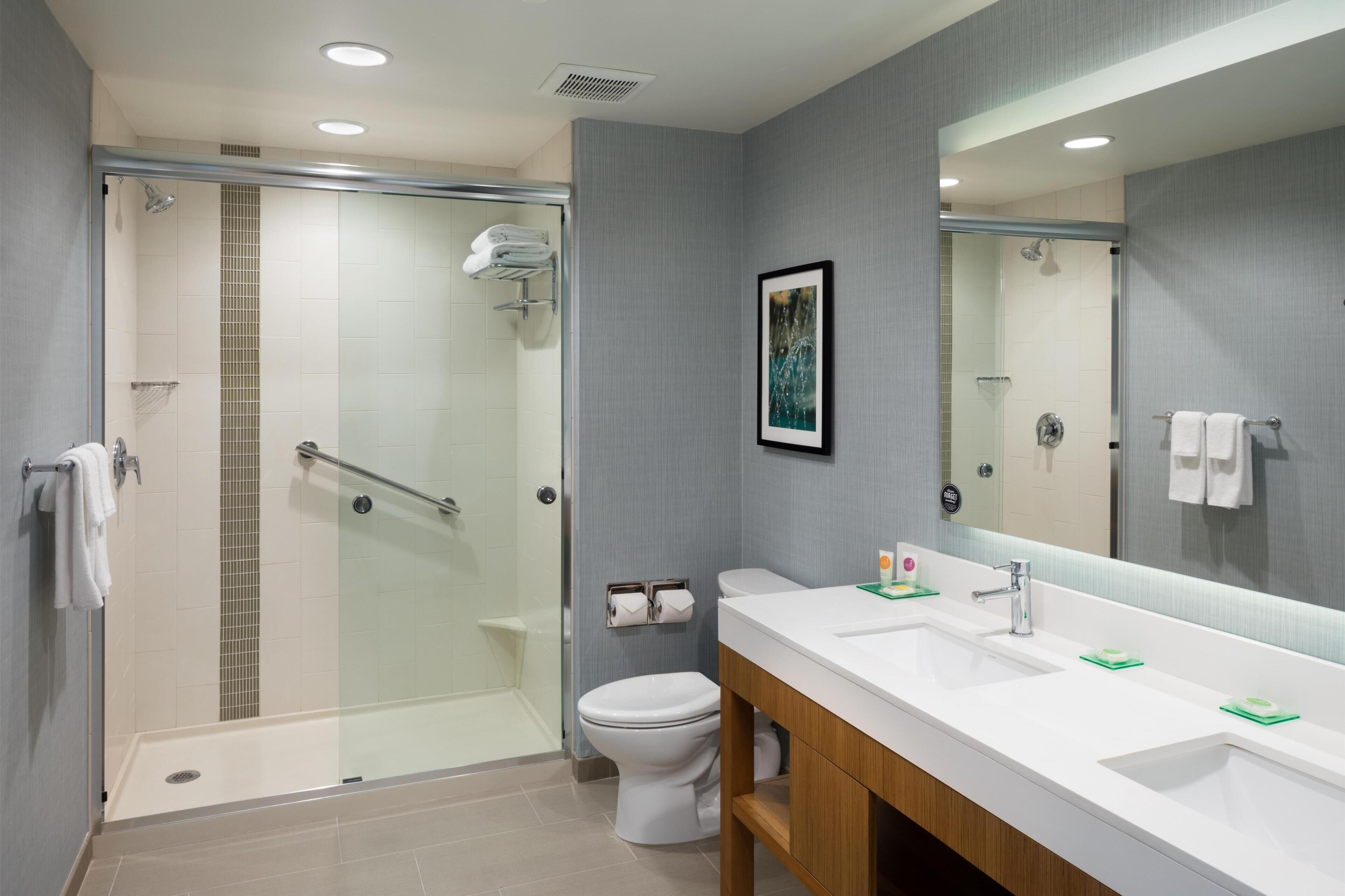 A modern bathroom with a glass-enclosed shower, a white toilet, and a double sink vanity with a large mirror.