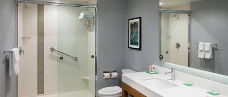 A modern bathroom with a glass-enclosed shower, a white toilet, and a double sink vanity with a large mirror.