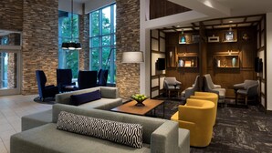 Un vestíbulo moderno con paredes de piedra, ventanas amplias y una variedad de zonas de estar, incluyendo sofás y sillones.