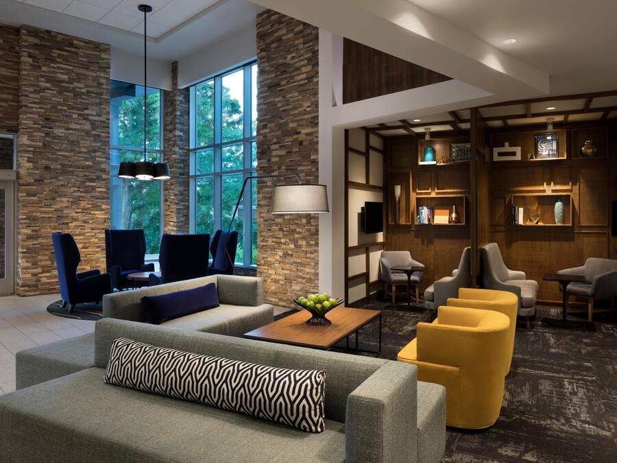 Un vestíbulo moderno con paredes de piedra, ventanas amplias y una variedad de zonas de estar, incluyendo sofás y sillones.