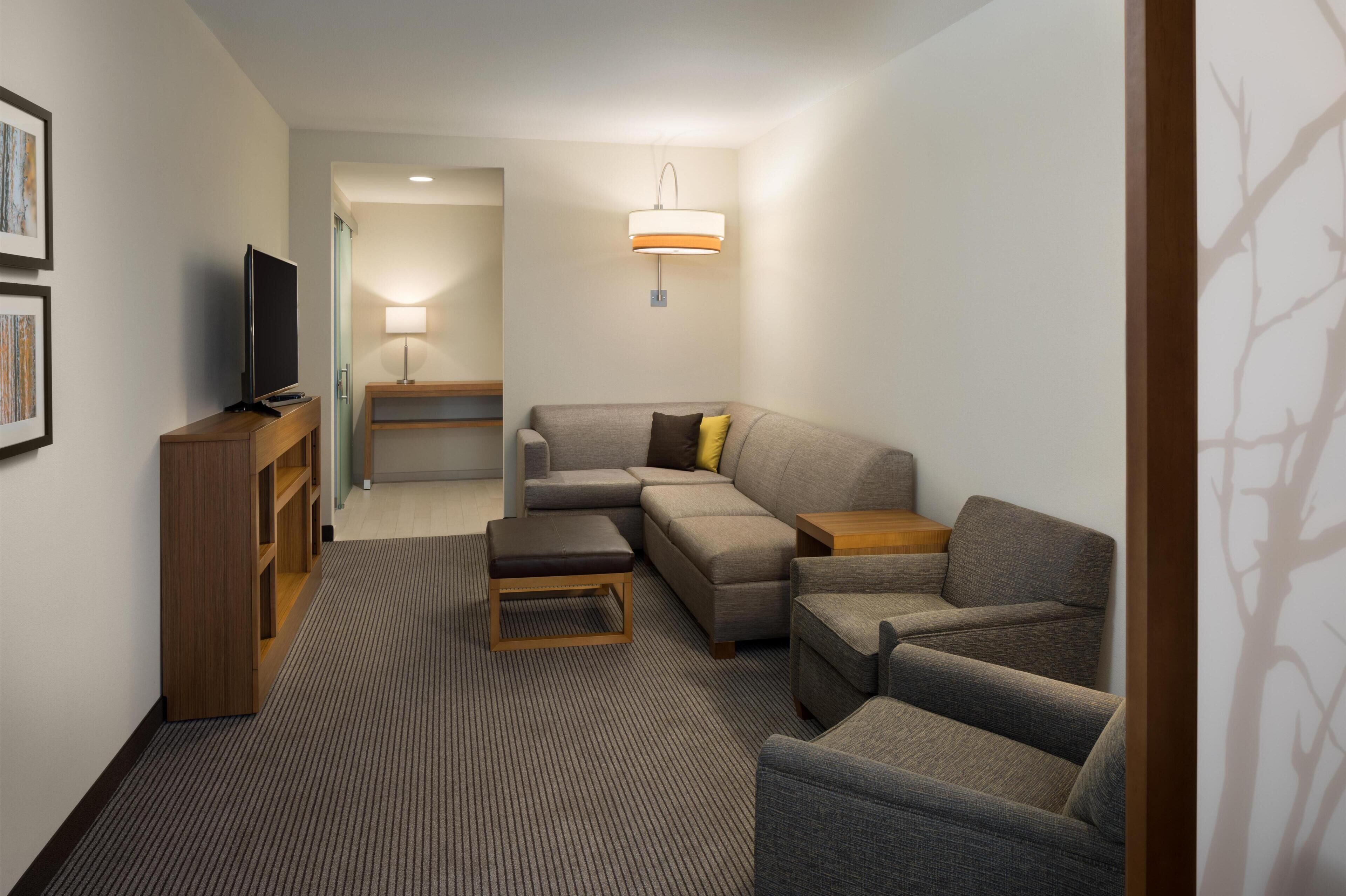 A modern living room with a sectional sofa, a flat-screen TV, a wooden cabinet, a lamp, and a patterned rug.