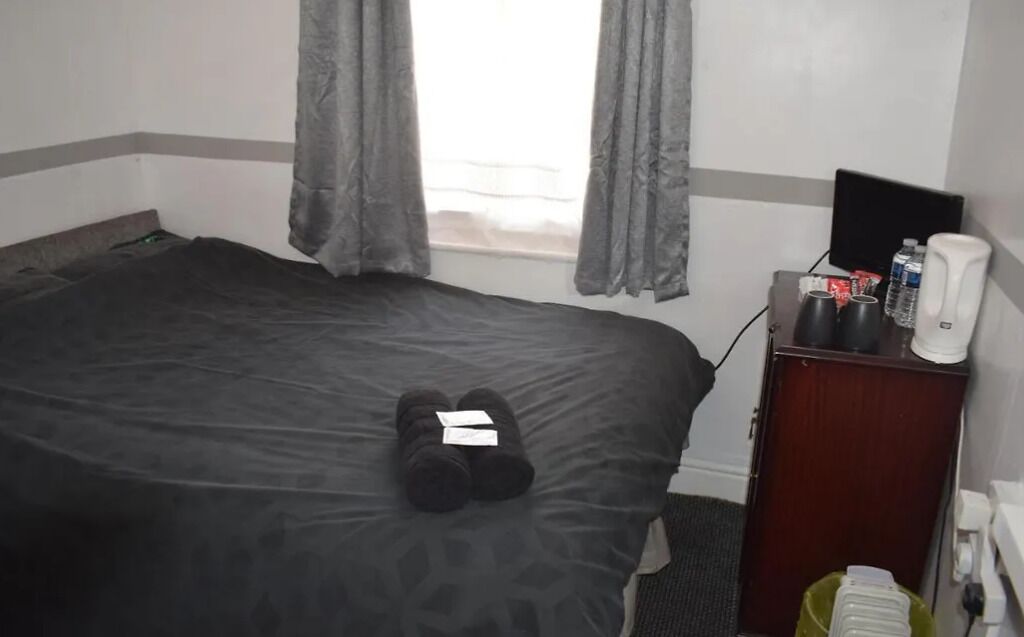 A hotel room with a bed, a desk with a computer, and a window with curtains.
