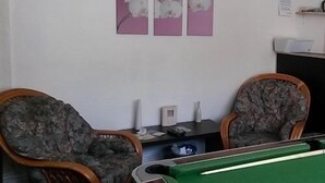 A room with a pool table, two patterned chairs, a small table with a bottle, and wall art. - Nelcon Hotel (Blackpool)
