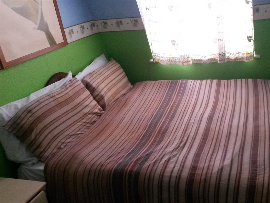 A room with a bed, pillows, a nightstand, and a window with a curtain.