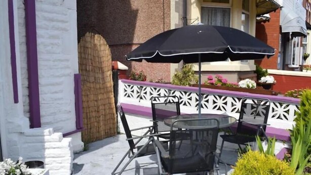 An outdoor patio with a round table and chairs, a black umbrella, and a decorative white fence. - Nelcon Hotel (Blackpool)