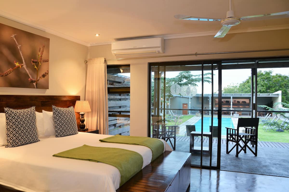 Une chambre d’hôtel avec un grand lit, un ventilateur de plafond et une vue sur une piscine et un espace de détente extérieur.