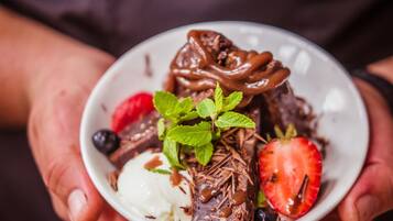 A person holding a bowl of dessert with chocolate, strawberries, and mint.