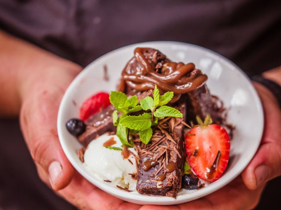A person holding a bowl of dessert with chocolate, strawberries, and mint.