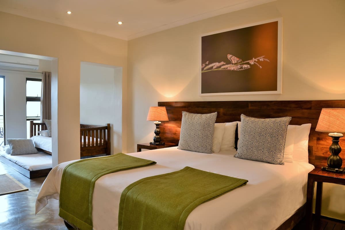 Une chambre d’hôtel avec un grand lit, deux tables de chevet avec des lampes, une œuvre d’art accrochée au mur et un balcon avec une chaise.