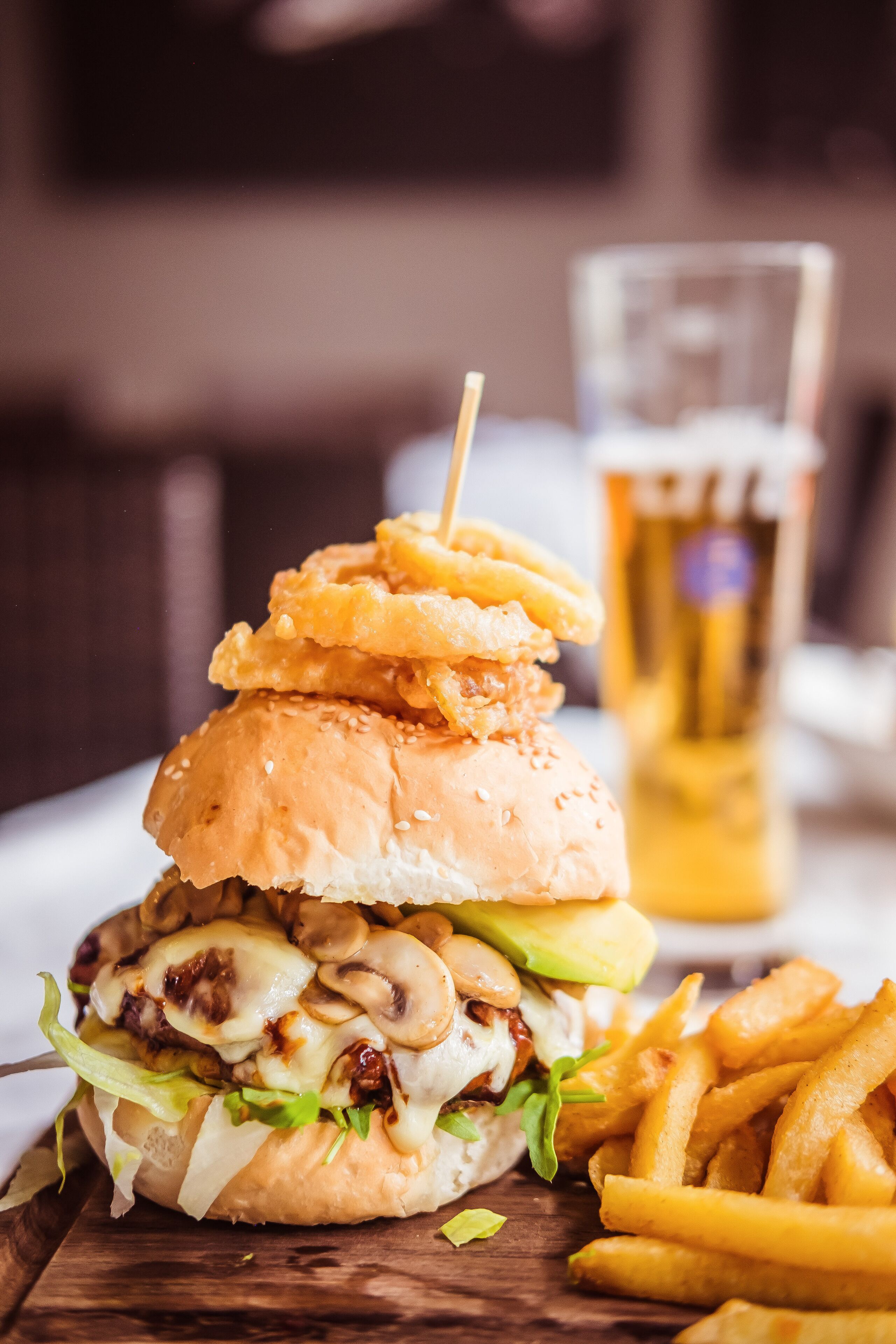 A burger with a bun, lettuce, cheese, and mushrooms, accompanied by fries and a glass of beer.