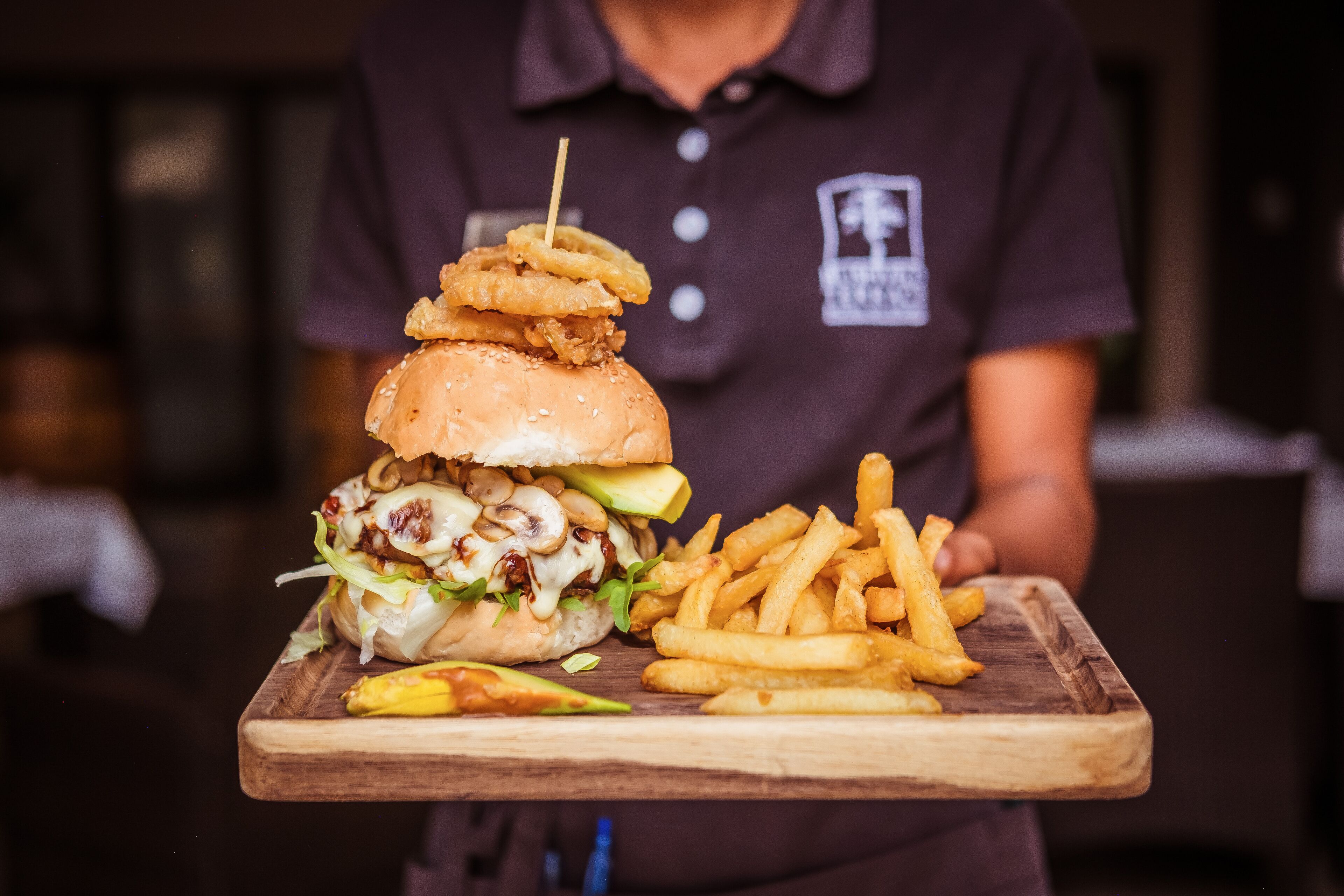 A person holding a tray with a burger, fries, and a banana.