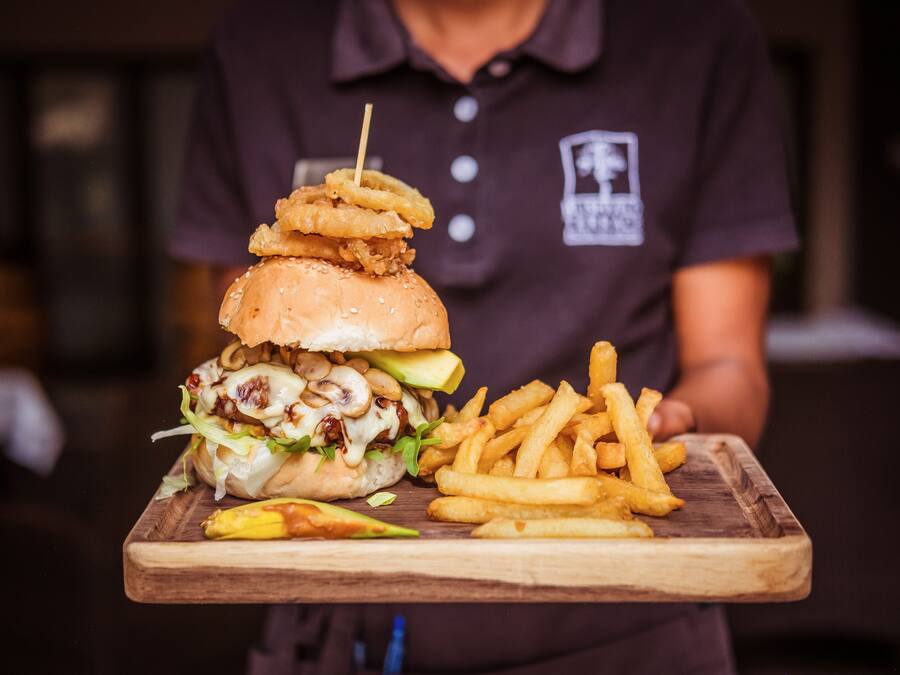 A person holding a tray with a burger, fries, and a banana.