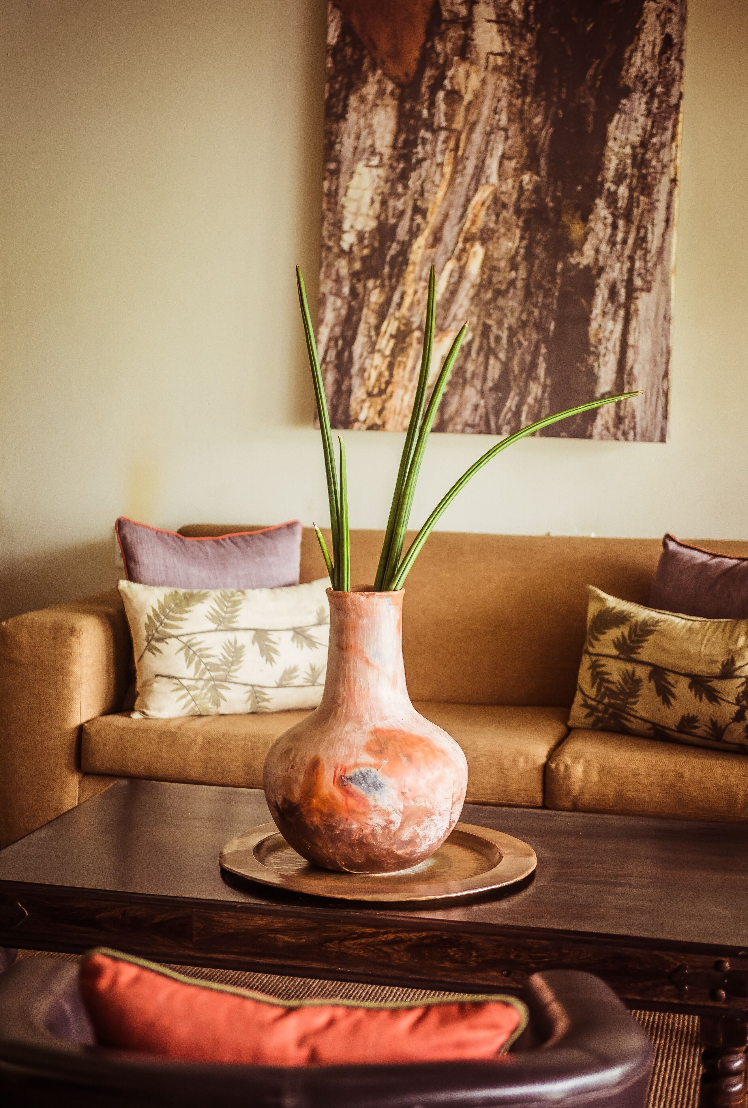Un salon avec un canapé marron, une table basse ronde en bois et un vase contenant des plantes vertes.