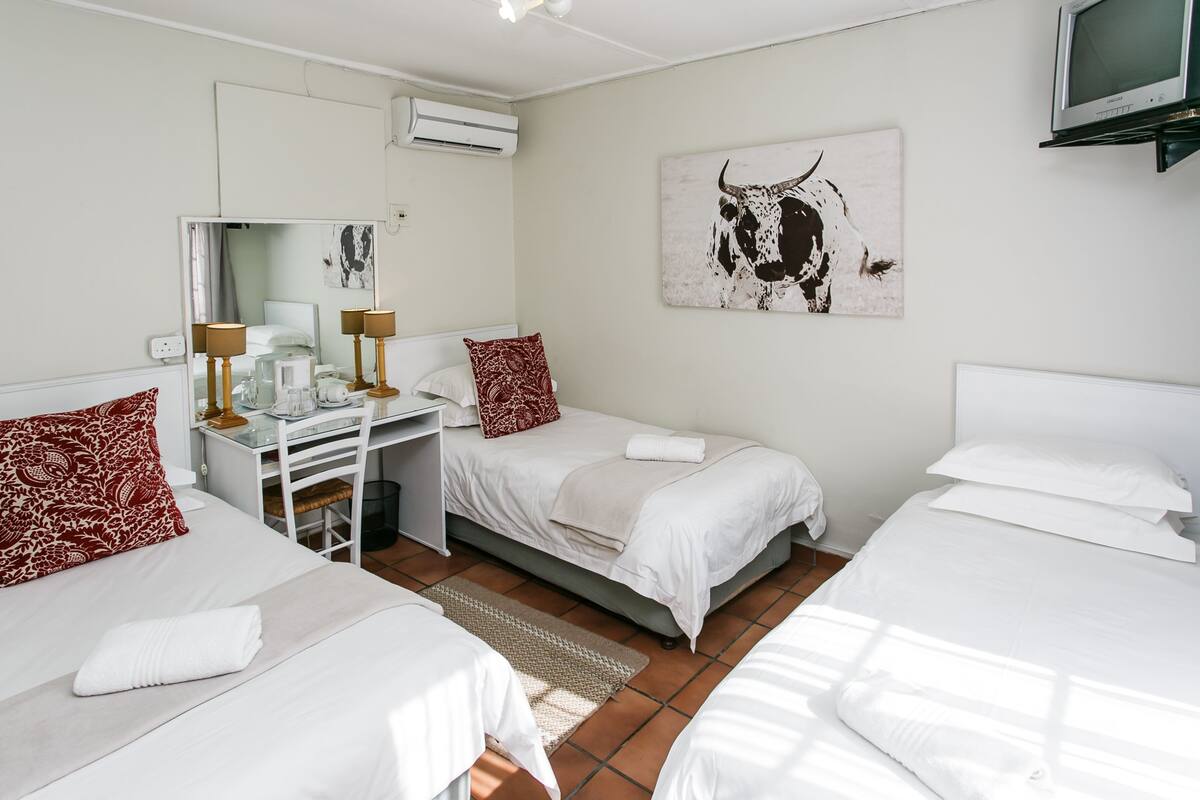 A hotel room with two beds, a desk with a chair, a TV, and a bull painting on the wall.
