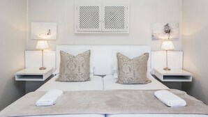 A double bed with two nightstands, each with a lamp and a small table. There are two pillows on the bed, and a blanket is folded at the foot of the bed. - Wagon Wheel Country Lodge (Beaufort West)
