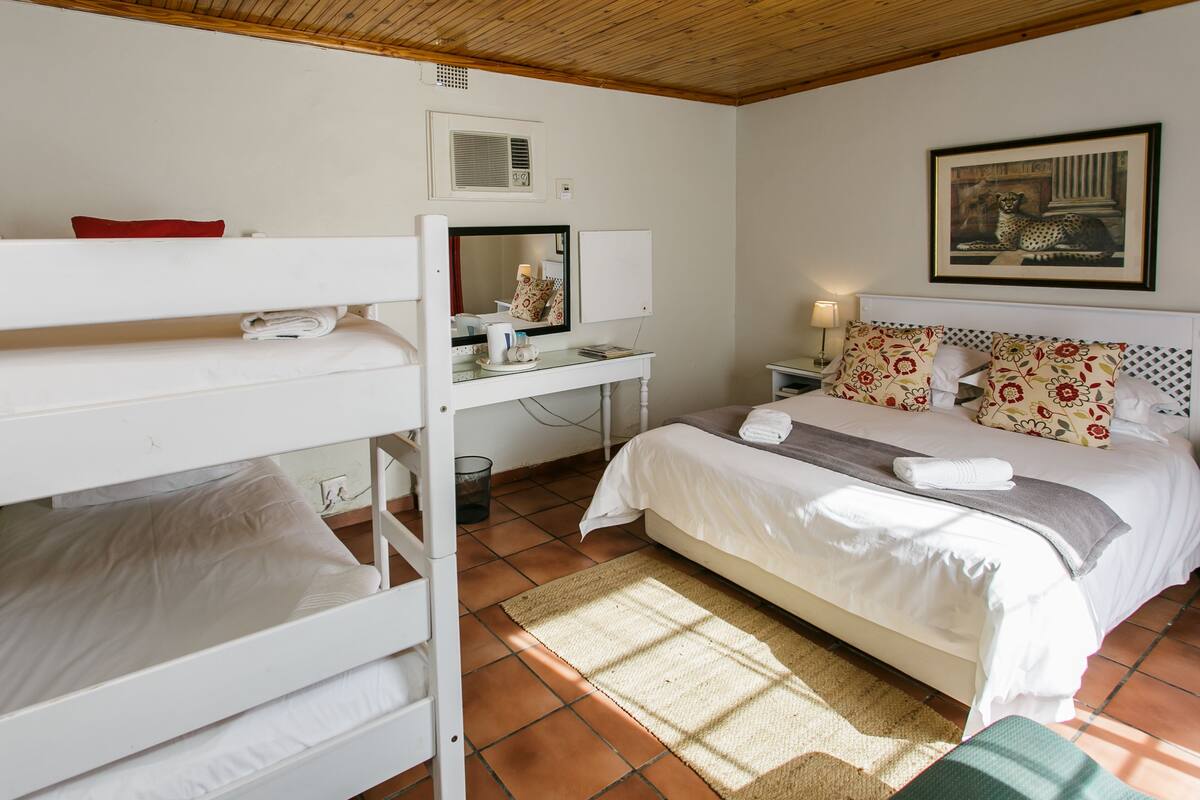 A bedroom with a bunk bed, a desk with a mirror, a bed with a floral headboard, and a painting of a leopard.