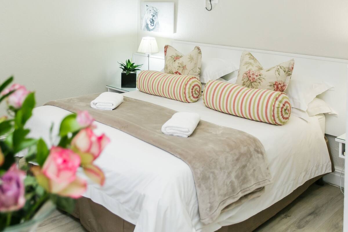 A neatly made bed with striped pillows, a beige throw blanket, and a white duvet.