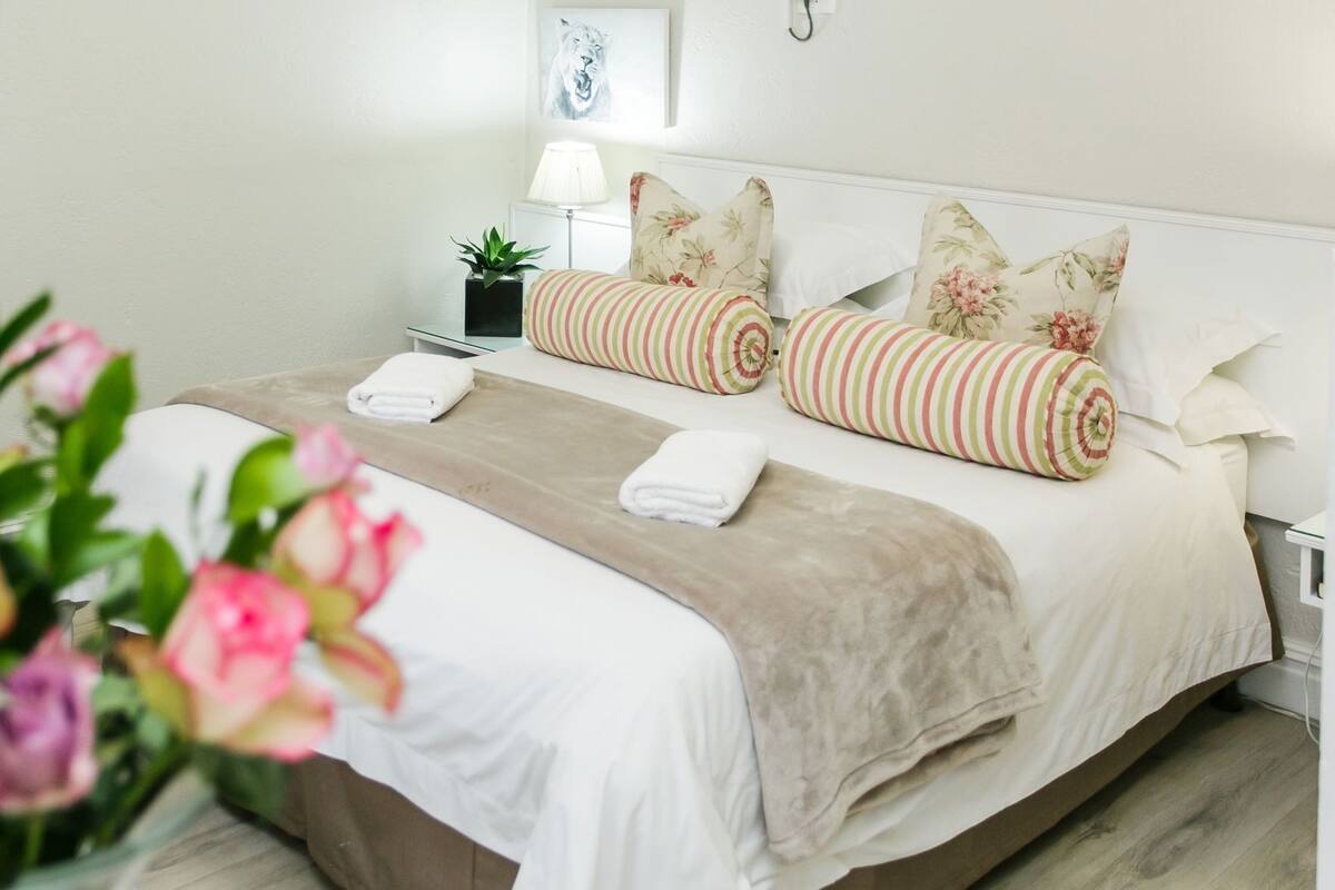 A neatly made bed with striped pillows, a beige throw blanket, and a potted plant beside the bed.