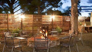 An outdoor patio with metal chairs, a fire pit, and a stone oven. - Wagon Wheel Country Lodge (Beaufort West)