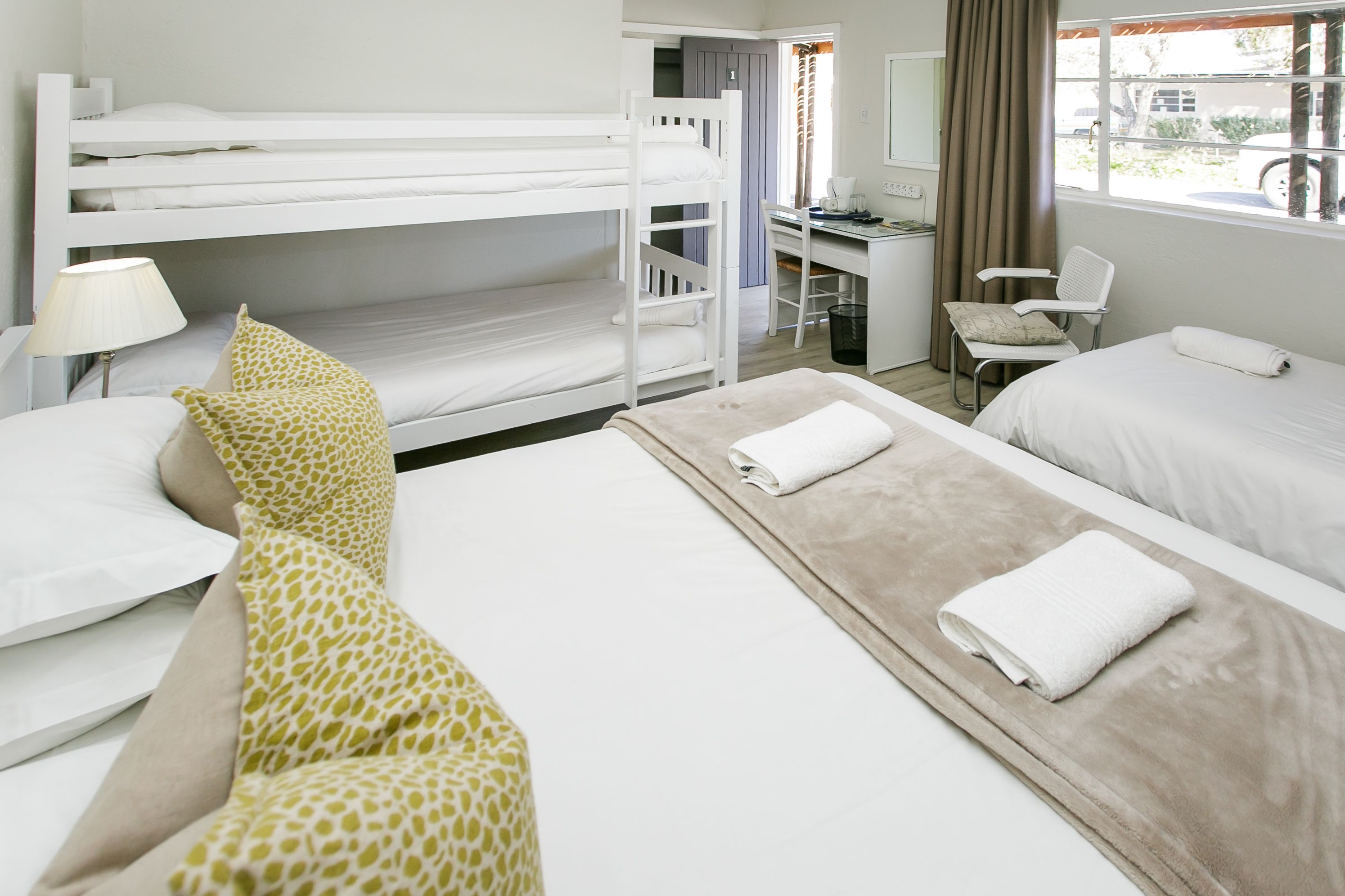 Une chambre d’hôtel avec des lits superposés, un bureau, une chaise et une fenêtre avec des rideaux.