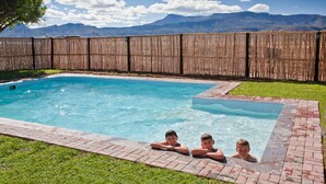 A rectangular swimming pool with a brick border and a wooden fence in the background. - Wagon Wheel Country Lodge (Beaufort West)