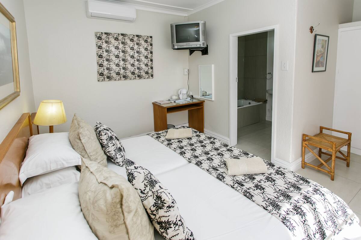 A hotel room with a bed, bedside table, lamp, TV, and a small wooden chair.