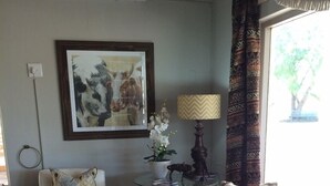 A living room with wicker furniture, a zebra rug, a framed artwork, a lamp, and a window with curtains. - Wagon Wheel Country Lodge (Beaufort West)