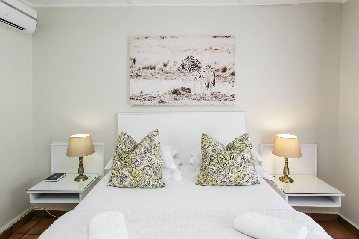 A hotel room with a bed, two bedside tables with lamps, patterned pillows, and a wall-mounted zebra painting.