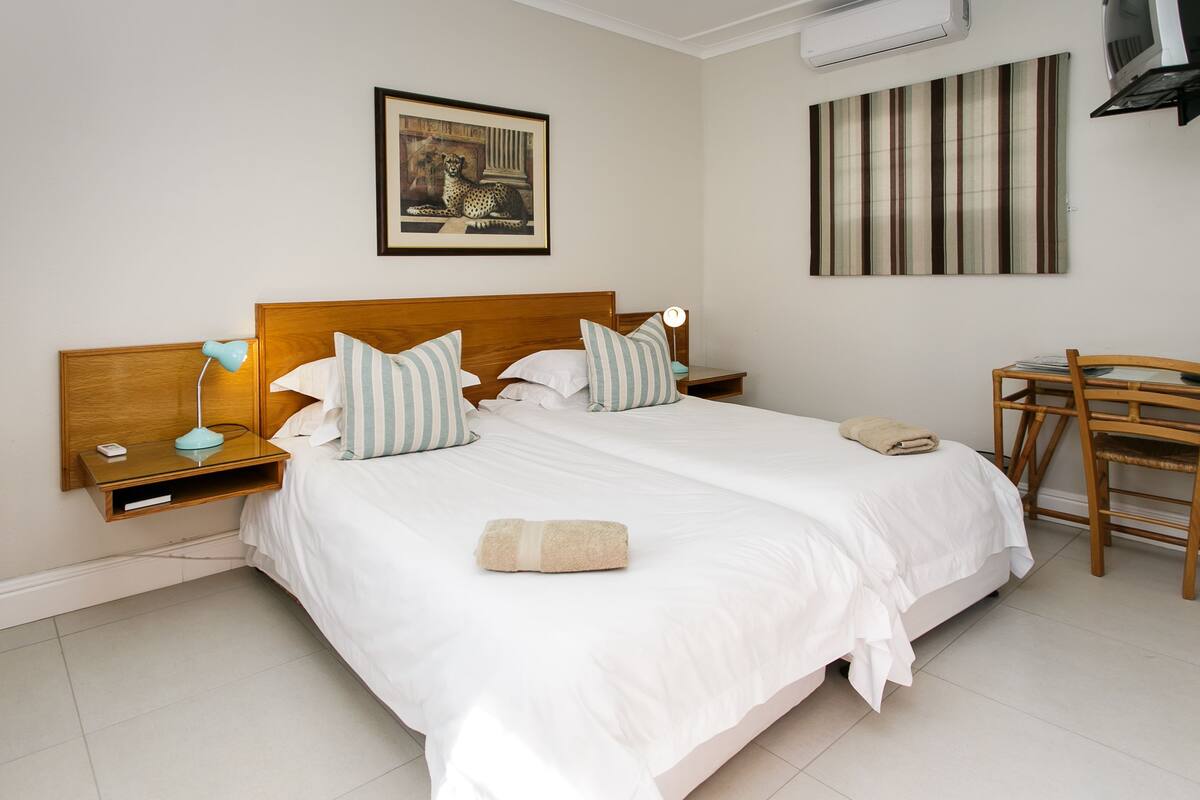 A neatly made bed with white linens, two bedside tables with lamps, a framed picture above the bed, and a striped artwork on the wall.