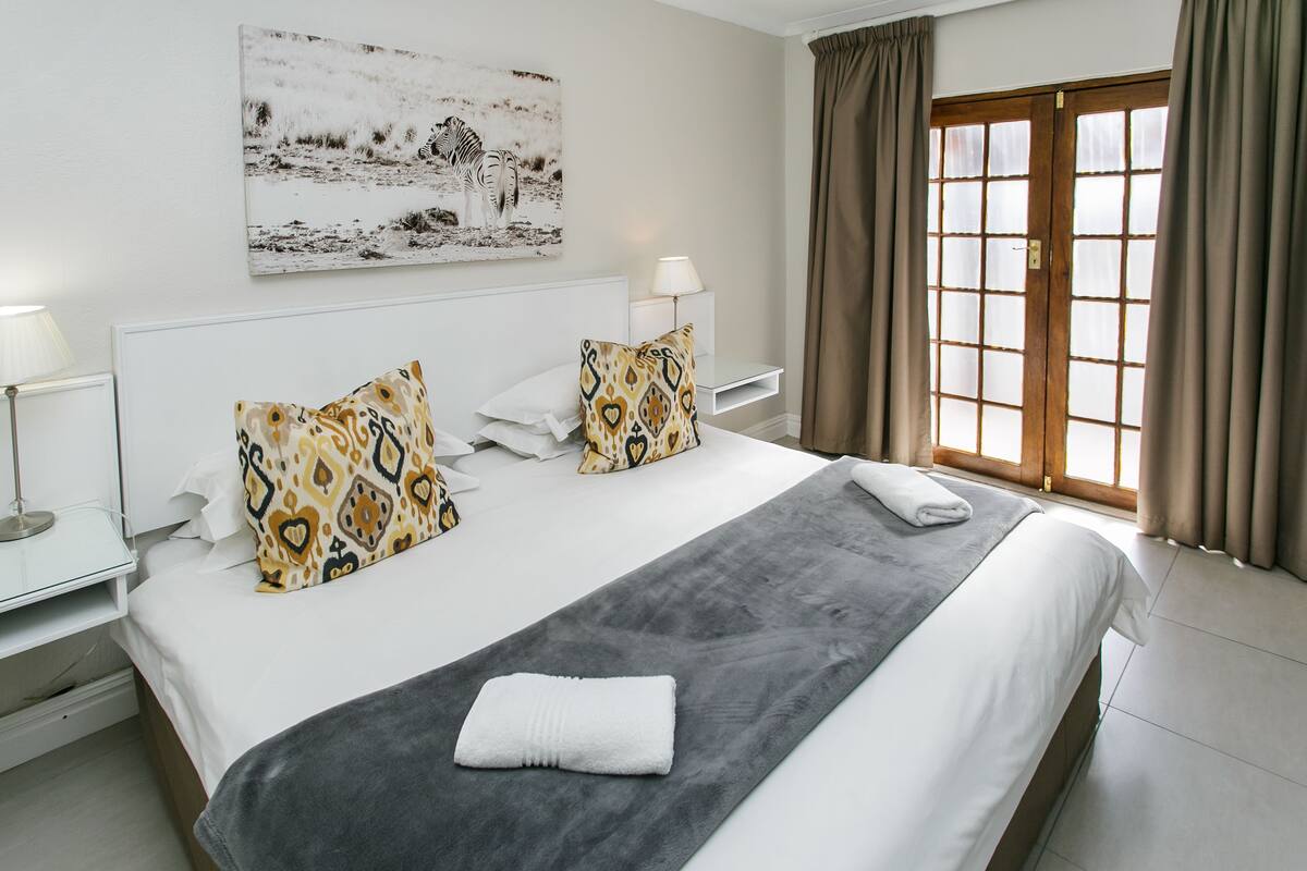 A neatly made bed with patterned pillows, a bedside lamp, and a window with curtains.