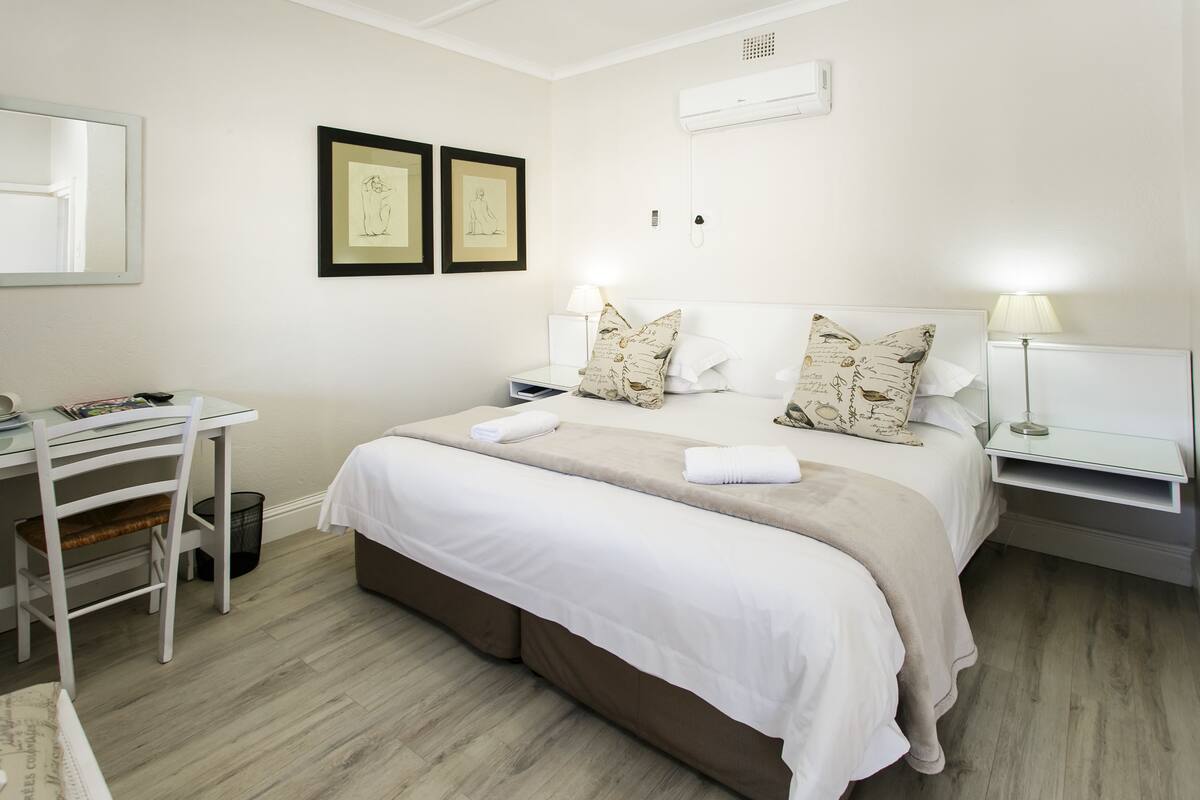 A hotel room with a bed, bedside tables, a desk, and a chair.