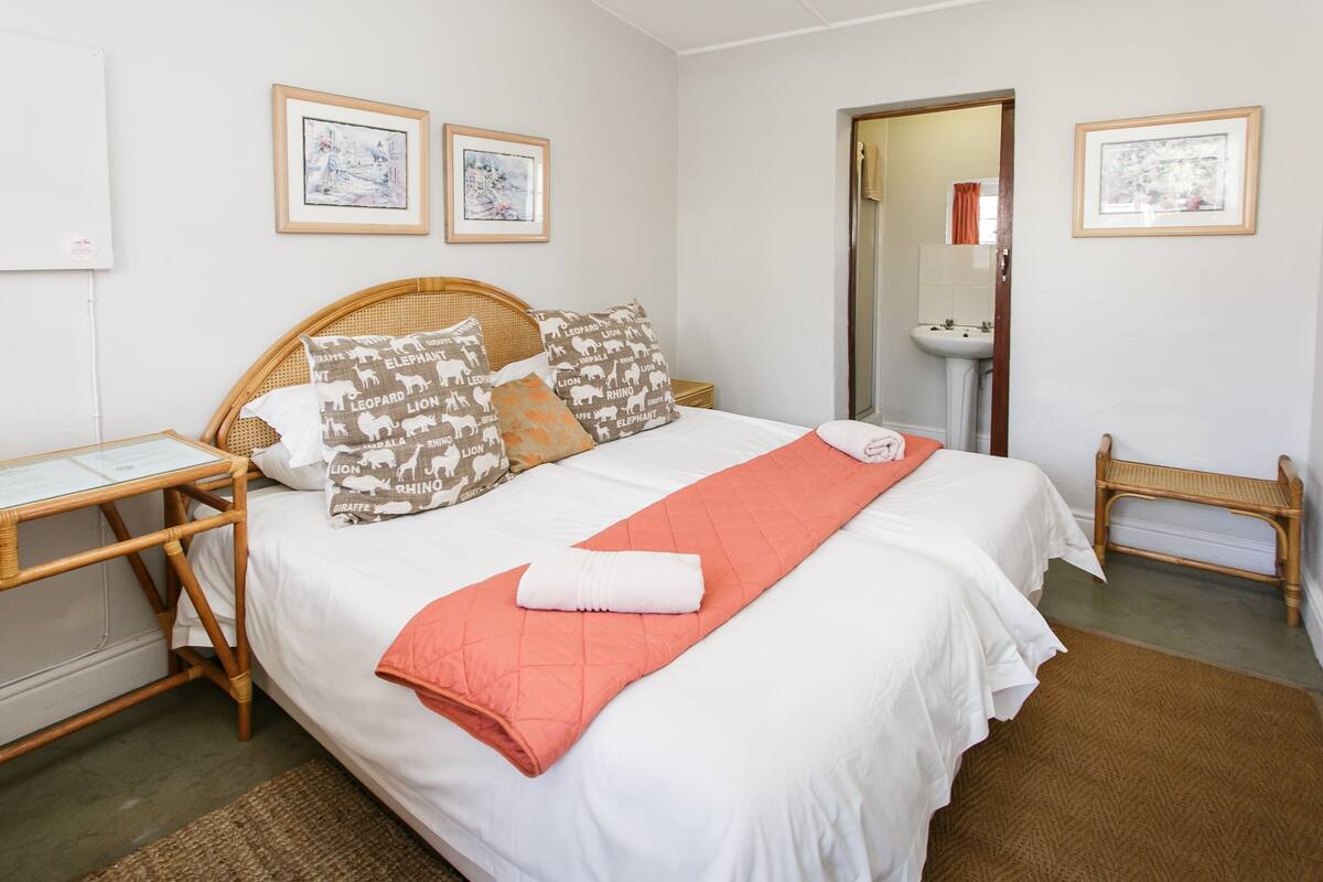 A neatly arranged bedroom with a bed, bedside tables, and a bathroom visible through an open door.