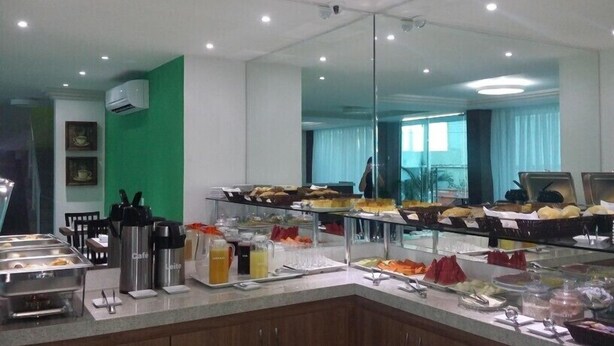 A buffet setup with various food items, a coffee station, and a mirror reflecting the room. - Gaia Suites Macaé (Macaé)