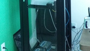 A computer tower with a glass front, cables, and a power strip on a desk. - Gaia Suites Macaé (Macaé)