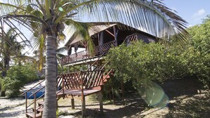 Een bungalow met rieten dak, houten balkonnes en een trap naar een terras.