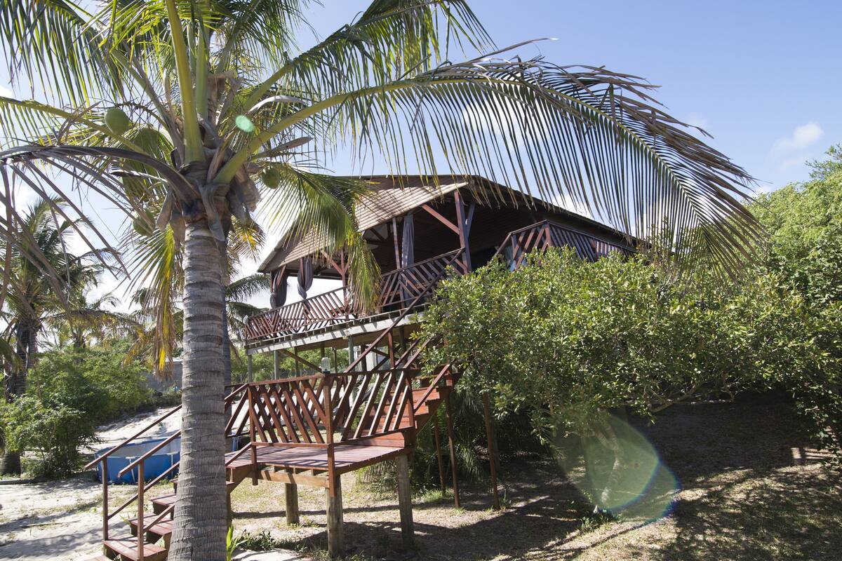 Een bungalow met rieten dak, houten balkonnes en een trap naar een terras.