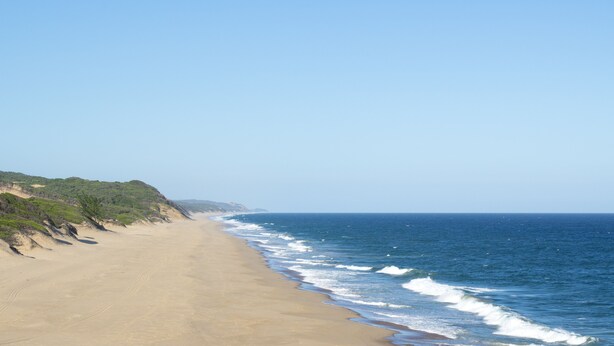 Een breed zandstrand met zachte golven en een heldere lucht.